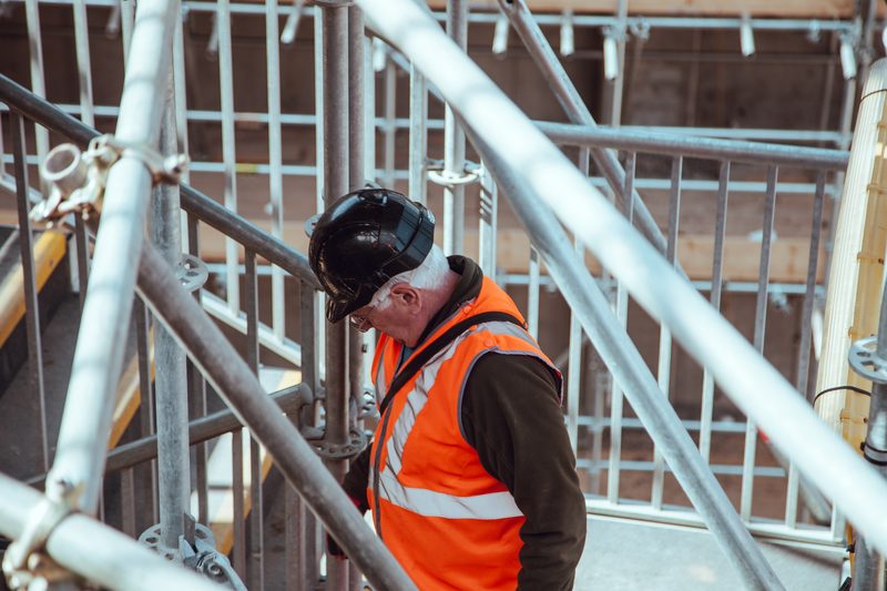 Een bouwmedewerker aan het werk tussen steigers op een bouwplaats.